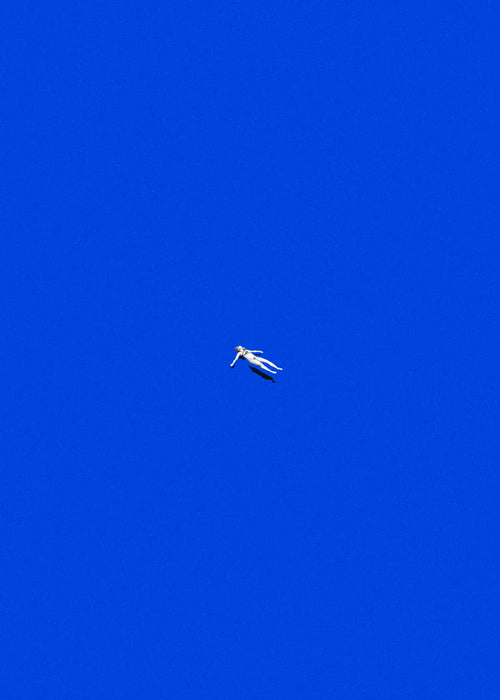 Minimalistisk plakat med svævende figur mod blå himmel